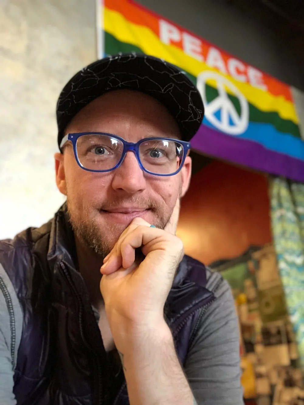 Daniel McCall in his blue glasses, smiling in front of a PEACE flag